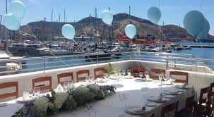 Mesa de celebración con decoración de globos azules y vista al puerto