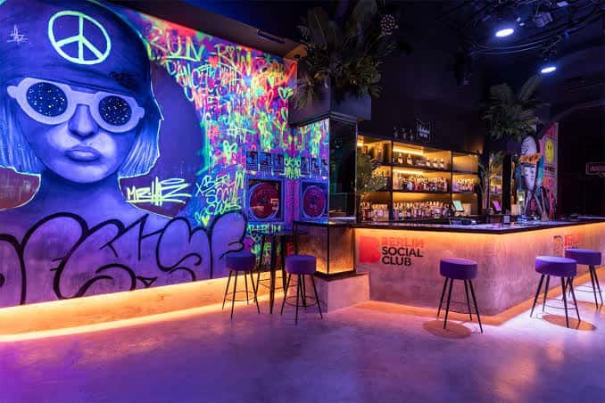 Interior del Berlin Social Club con barra iluminada y mural de graffiti colorido