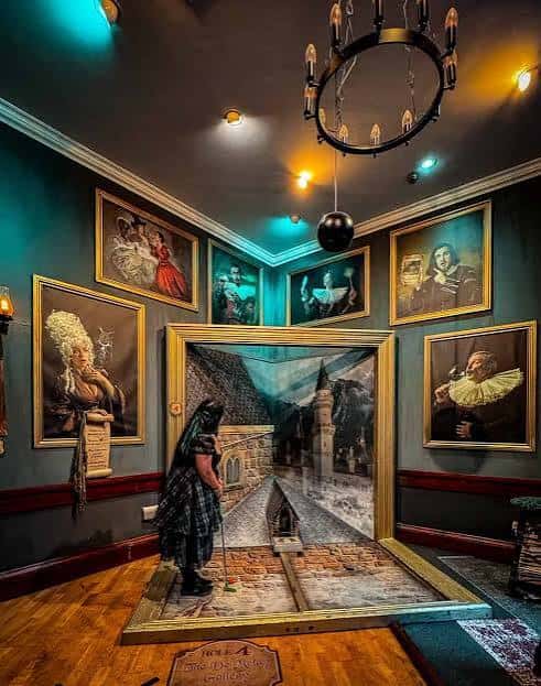 Jugadora en el hoyo temático de castillo con pintura mural y retratos enmarcados