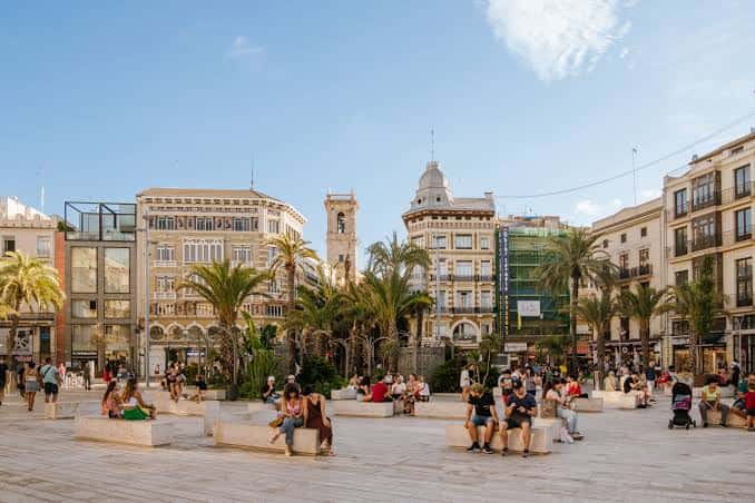 Plaza de la Reina con personas relajándose en bancos y palmeras bajo el sol