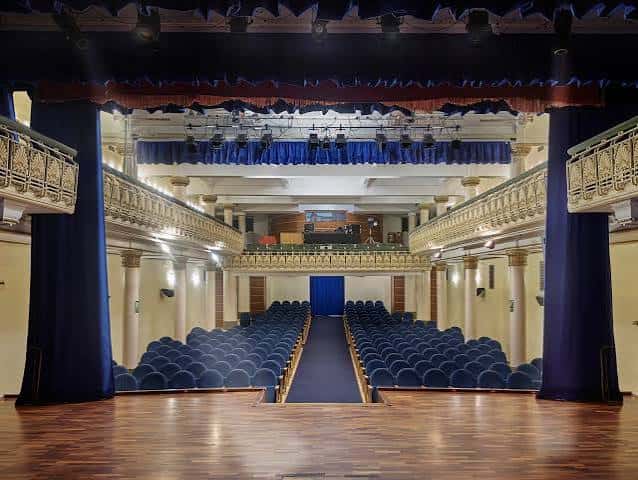 Interior del auditorio con butacas azules y escenario con cortinas
