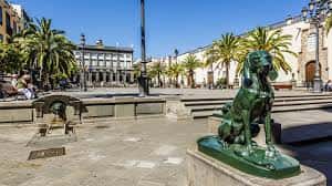 Plaza de Santa Ana con esculturas de perros en primer plano, palmeras y edificios coloniales al fondo bajo un cielo despejado