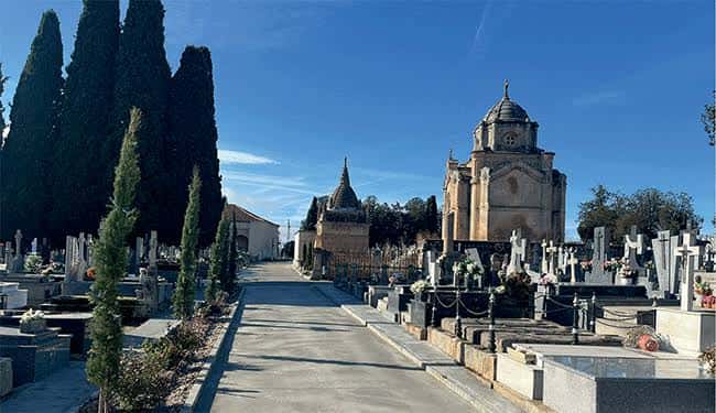 Vista panorámica del Cementerio San Carlos Borromeo con capilla y cipreses bajo cielo azul