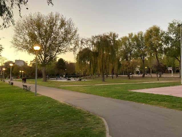 Paseo arbolado del parque al atardecer con bancos y farolas encendidas