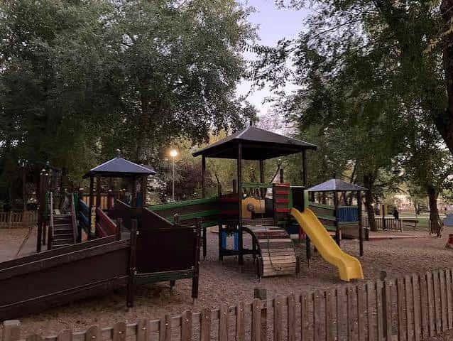 Zona de juegos infantiles con toboganes y estructuras de madera bajo árboles