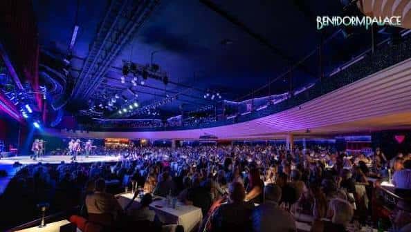 Escenario iluminado con artistas y audiencia en ambiente festivo