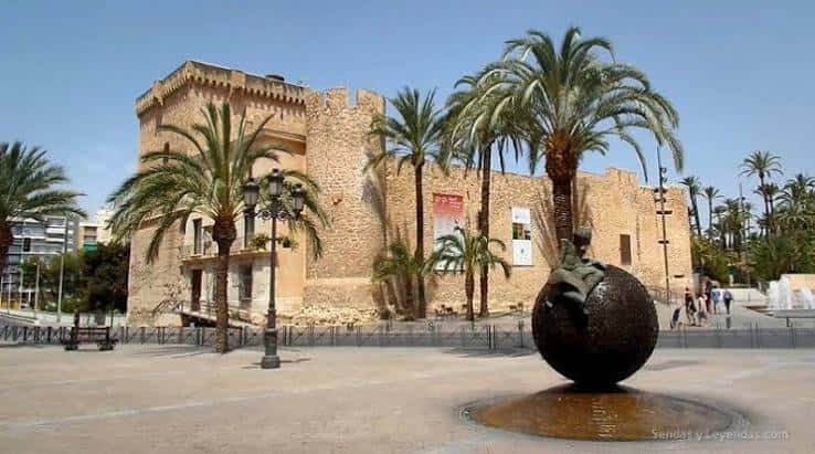 Fachada del palacio con escultura y palmeras en primer plano