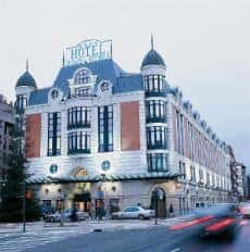 Fachada del hotel al atardecer con luces encendidas y tráfico borroso