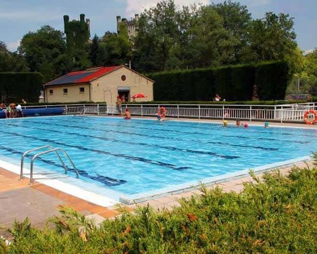 Vista general de la piscina descubierta de Las Caldas con personas disfrutando del agua y el entorno verde