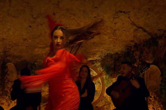 Escena de baile flamenco en vivo dentro de la cueva, con una bailarina en vestido rojo y músicos de fondo bajo iluminación cálida