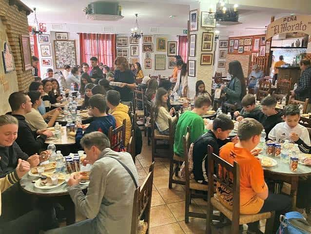 Interior de la Peña Flamenca El Morato durante una visita escolar, con jóvenes sentados en mesas y decoración tradicional en las paredes