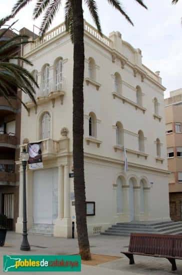 Fachada lateral de la Escola del Mar con palmera y banco en primer plano