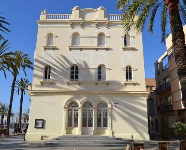 Vista frontal de la Escola del Mar en Badalona con palmeras y cielo azul