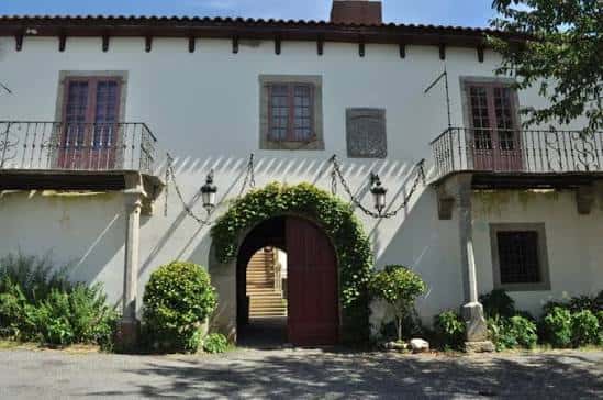 Fachada principal del Pazo de Tor con balcones y puerta arqueada decorada con vegetación