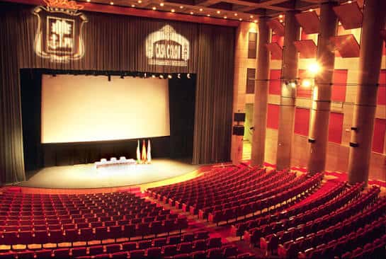 Interior del auditorio de la Casa Colón con escenario y butacas rojas