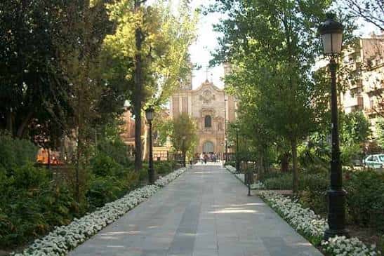 Paseo central del jardín con sendero empedrado y fachada de iglesia al fondo