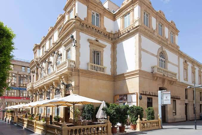 Fachada exterior del Teatro Cervantes en Almería con terraza y sombrillas