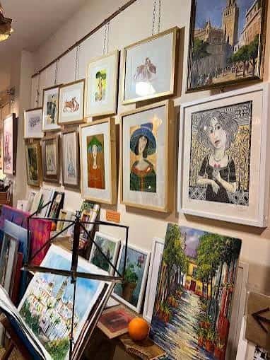 Pared de la galería con múltiples cuadros enmarcados y obras de arte variadas