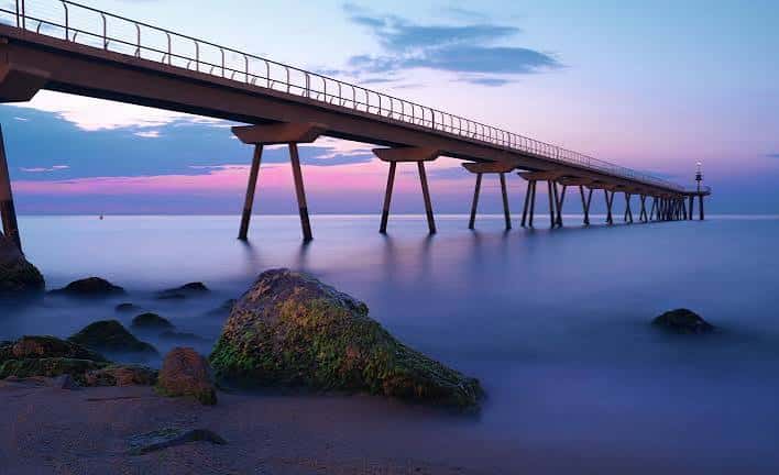 Vista del Pont del Petroli al atardecer con cielo rosado y mar en calma