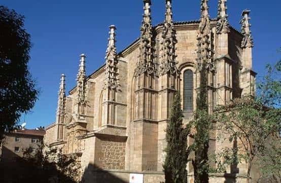 Ángulo lateral de la iglesia con torres y ventanas góticas bajo cielo azul