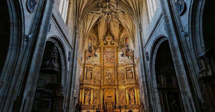 Interior de la iglesia con retablo dorado y bóvedas de crucería