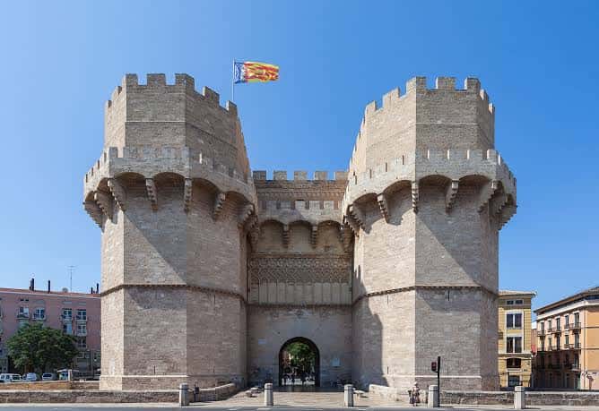 Vista frontal de la Plaza de la Crida con la puerta de los Hierros bajo el cielo azul