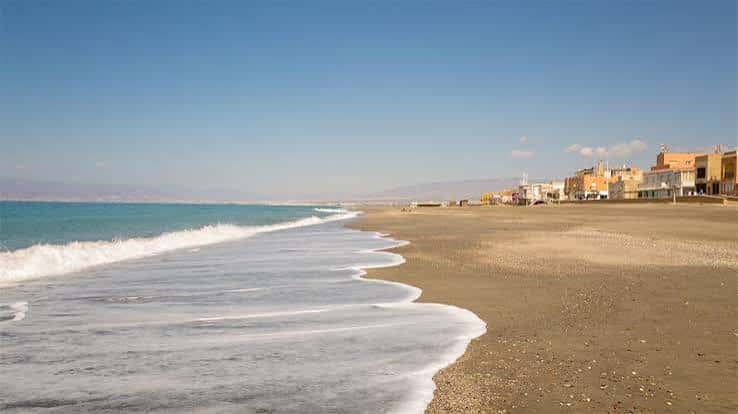 Vista panorámica de la playa con olas suaves y edificios costeros al fondo