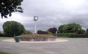 Monumento circular con fuente y césped rodeado de árboles en un día nublado