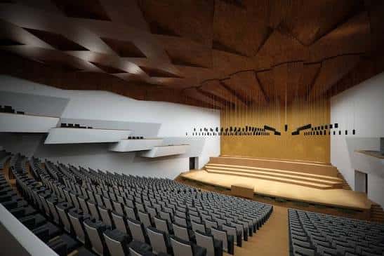 Vista del auditorio desde la platea hacia el escenario, destacando el diseño acústico del techo y los balcones laterales