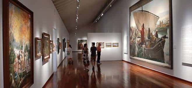 Interior de la sala de exposiciones con obras de arte enmarcadas y visitantes admirando las pinturas