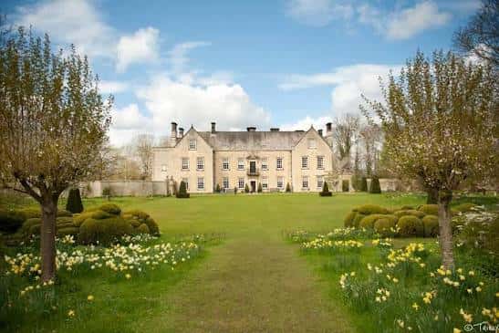 Vista frontal de Nunnington Hall en un día soleado, con jardines floridos y césped verde