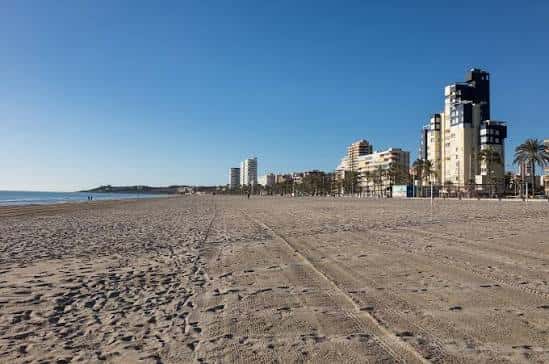 Vista panorámica de la Playa de San Juan con arena, edificios costeros y cielo despejado