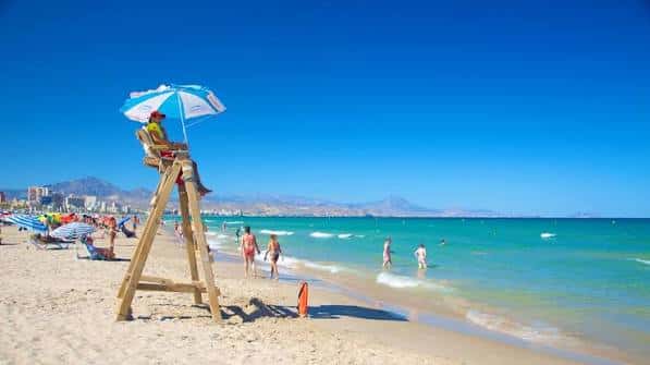 Guardavidas en torre de madera con sombrilla en la Playa de San Juan, bañistas y olas suaves
