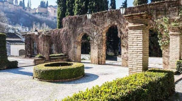 Jardines históricos del palacio con arcos de piedra, setos circulares y vistas al Albaicín al fondo