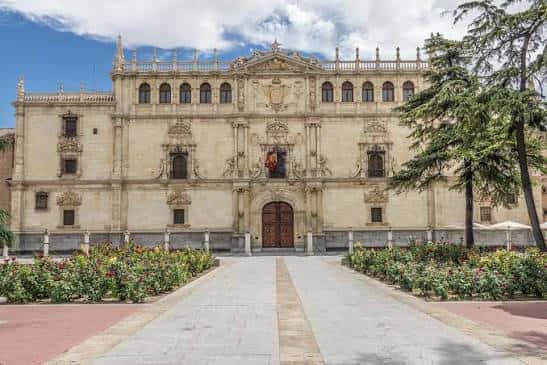 Fachada principal de la Universidad de Alcalá con jardín y cielo despejado
