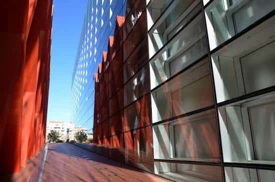 Detalle arquitectónico de la fachada con paneles de vidrio y elementos estructurales en color rojo óxido bajo luz solar directa