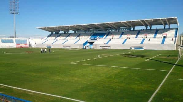 Vista panorámica del campo de fútbol con gradas azules y blancas bajo cielo despejado