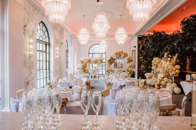 Sala de banquete preparada para boda con globos dorados y cristalería