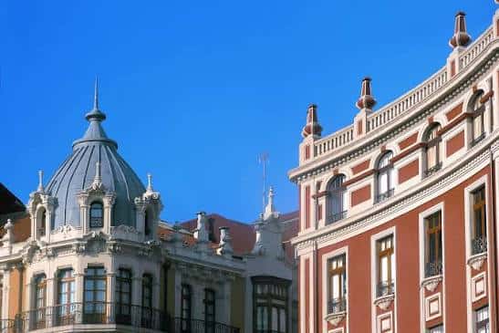 Fachadas de edificios modernistas en Gijón con detalles arquitectónicos y cúpulas bajo cielo azul