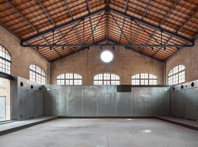 Interior del salón principal con techos de vigas metálicas y suelo de hormigón