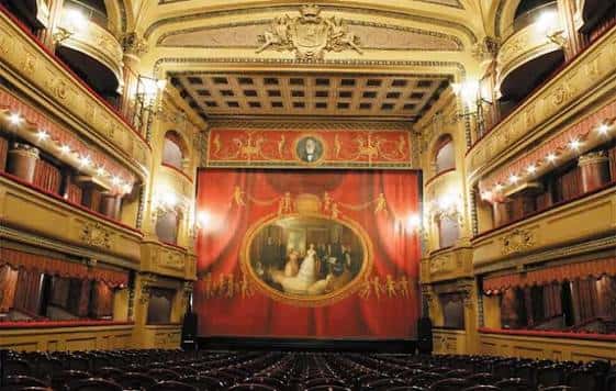 Interior del teatro con el telón rojo cerrado y el escenario listo para la función