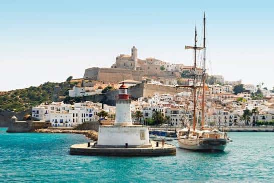 Vista panorámica de la ciudadela de Ibiza desde el puerto con el faro y un barco de vela