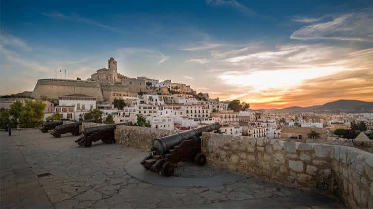 Paisaje de Dalt Vila con cañones históricos en primer plano y el atardecer