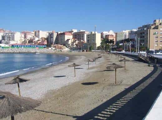 Playa de Benítez con sombrillas de paja y edificios costeros al fondo