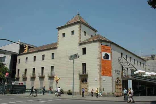 Vista exterior del edificio histórico del Centre d'Arts Santa Mònica con su fachada de piedra y torre