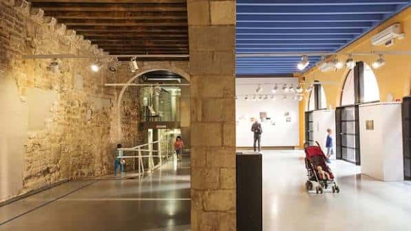Galería de exposiciones con paredes de piedra histórica y techos modernos
