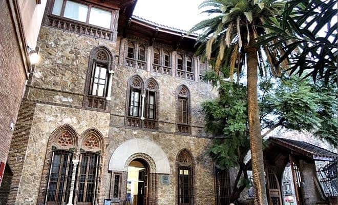 Edificio histórico de piedra con arquitectura gótica y palmeras en el patio