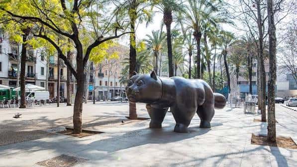 Escultura de oso en la Rambla del Raval con palmeras y edificios de fondo