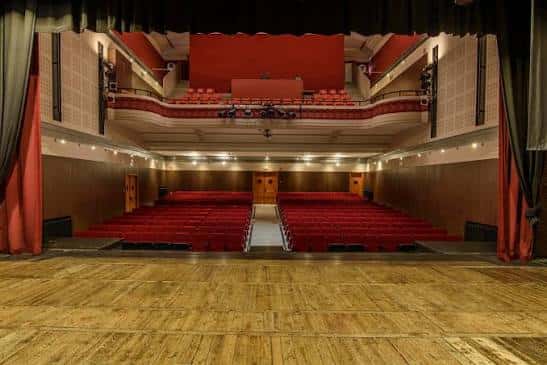 Interior del auditorio con butacas rojas y escenario de madera