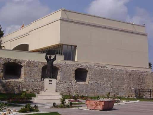 Vista exterior del Baluarte de los Mallorquines con fachada moderna y escultura frente a la muralla histórica